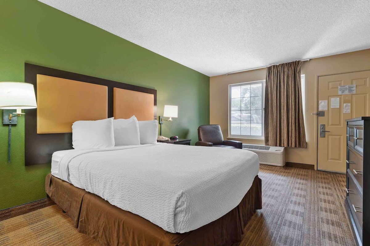 A hotel room with a large bed, two bedside lamps, a chair, a desk, a dresser, and a window with curtains.