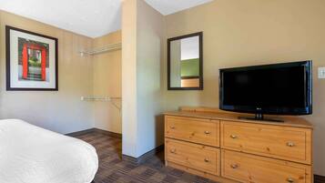 Een hotelkamer met een bed, een houten dressoir, een flatscreen televisie, een lijst met een afbeelding aan de muur en een spiegel.
