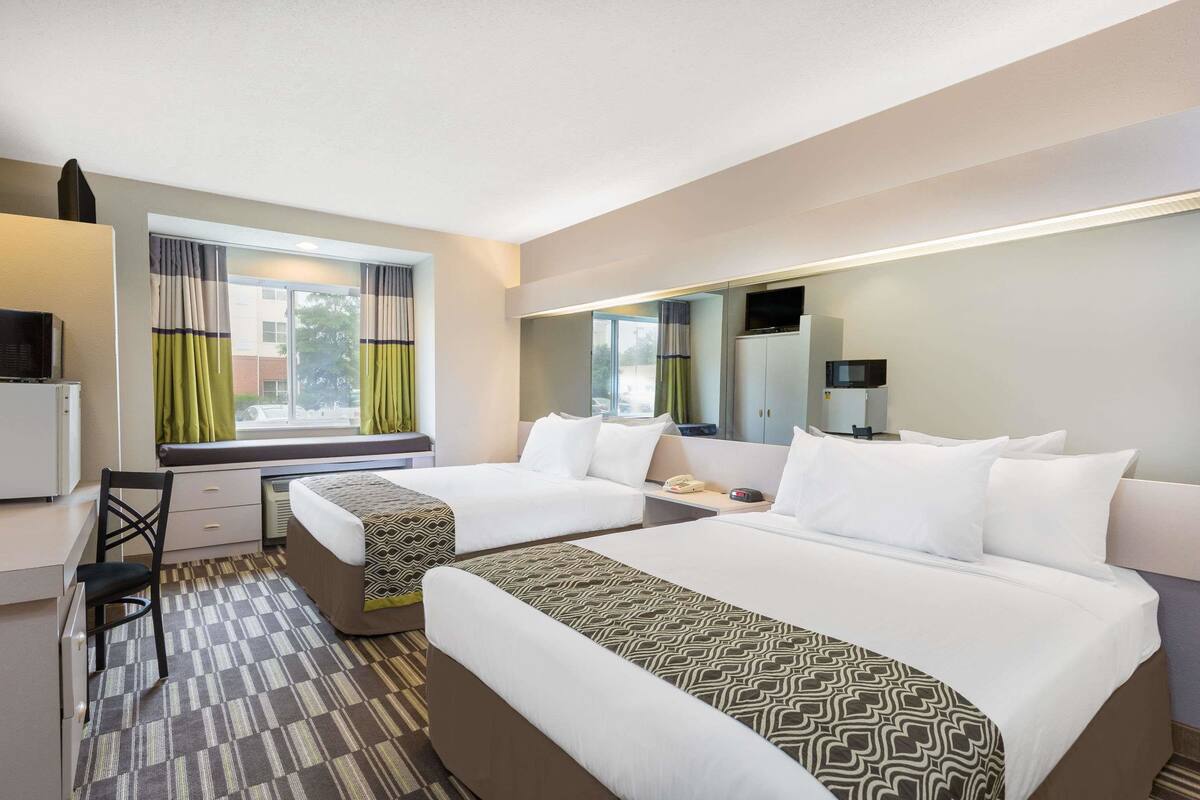 Une chambre d’hôtel avec deux lits, un bureau, une chaise, une télévision et une fenêtre avec des rideaux.