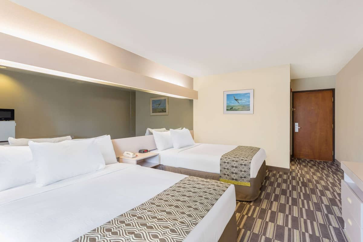 Une chambre d’hôtel avec deux lits, une table de chevet avec un téléphone, une lampe et un tableau au mur.