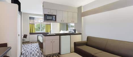 Habitación de hotel compacta con kitchenette, sofá y zona de comedor.