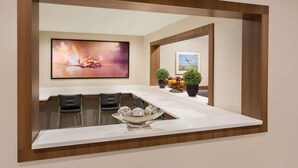 A modern kitchen with a white countertop, three bar stools, a large painting, and potted plants. - Microtel Inn & Suites by Wyndham Richmond Airport (Sandston)