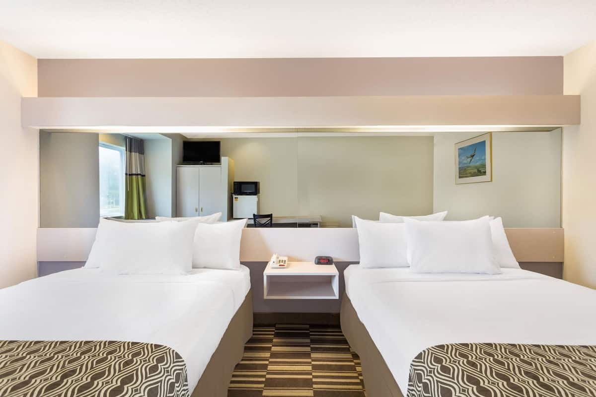 Une chambre d’hôtel avec deux lits, une petite table, un four à micro-ondes, une télévision et une fenêtre avec des rideaux.