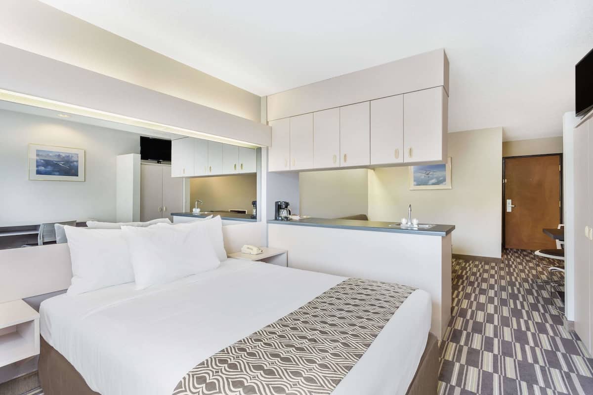 Une chambre d’hôtel comprenant un lit, un bureau, un miroir, une kitchenette et une salle de bain.