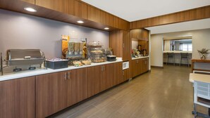 A modern kitchen area with wooden cabinets, a buffet setup, and a seating area with chairs and a table. - Microtel Inn & Suites by Wyndham Richmond Airport (Sandston)