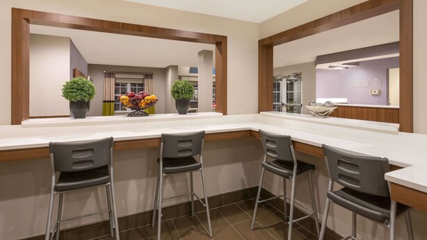 A modern kitchen with a white countertop, four bar stools, and two potted plants. - Microtel Inn & Suites by Wyndham Richmond Airport (Sandston)