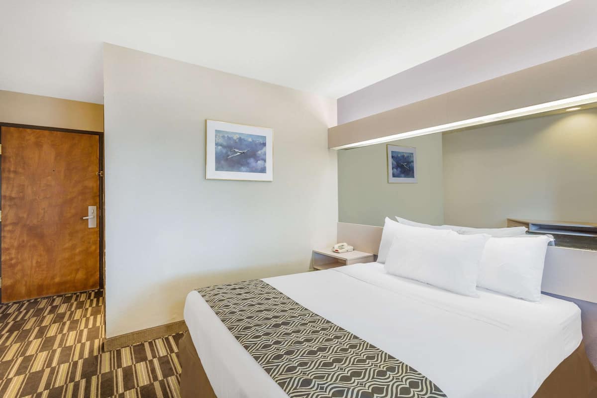 Une chambre d’hôtel avec un lit, une table de chevet, un miroir et une porte.