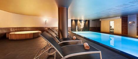 A modern indoor pool area with lounge chairs and a hot tub.