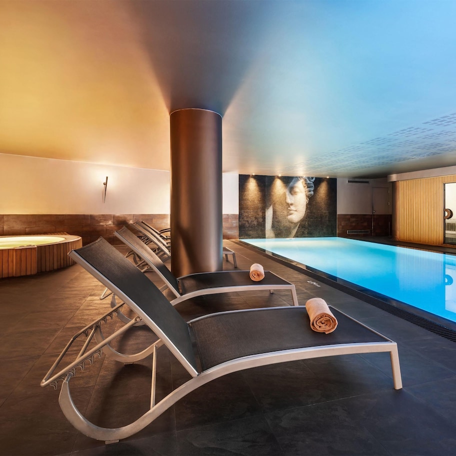 A modern indoor pool area with lounge chairs and a hot tub.