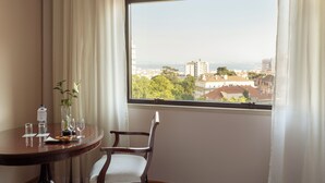 A room with a dining table set for two, a chair, a vase with flowers, and a view of a cityscape through a window. - Dom Pedro Lisboa Hotel, a member of Radisson Individuals (Lisbon)