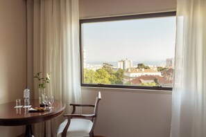 A room with a dining table set for two, a chair, a vase with flowers, and a view of a cityscape through a window. - Dom Pedro Lisboa Hotel, a member of Radisson Individuals (Lisbon)