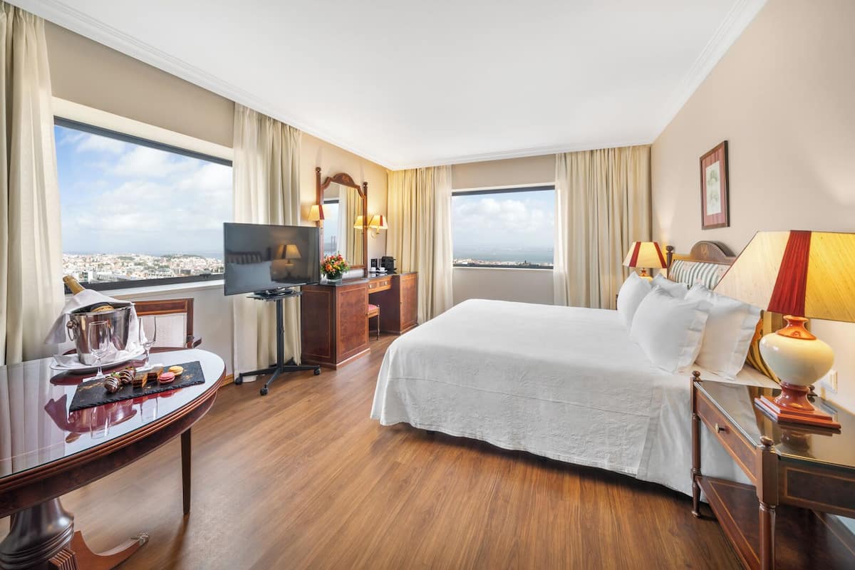 Habitación de hotel con cama, escritorio, televisor y vista a la ciudad.