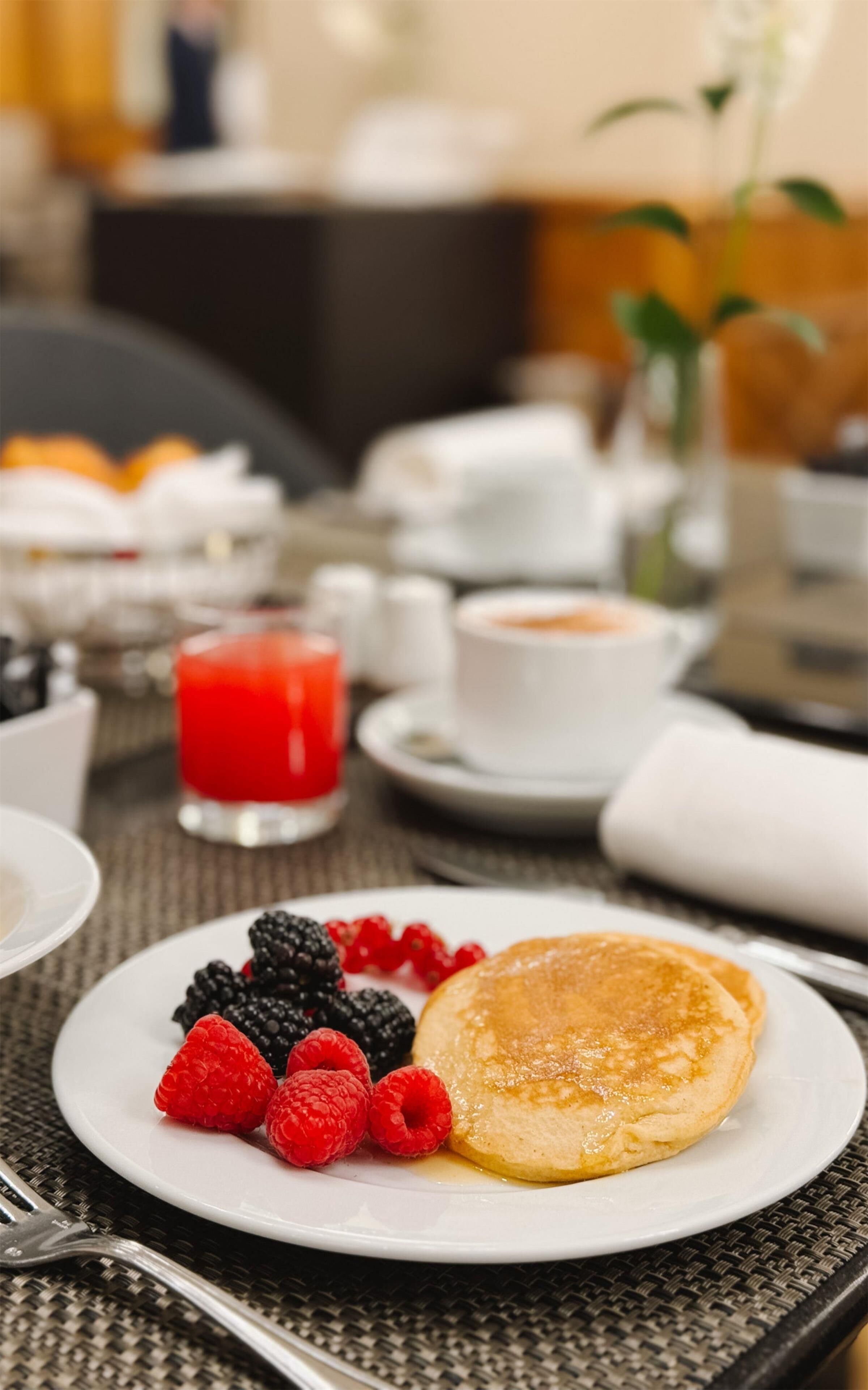 A breakfast setting with pancakes, berries, and a red drink on a table.