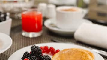 A breakfast setting with pancakes, berries, and a red drink on a table.