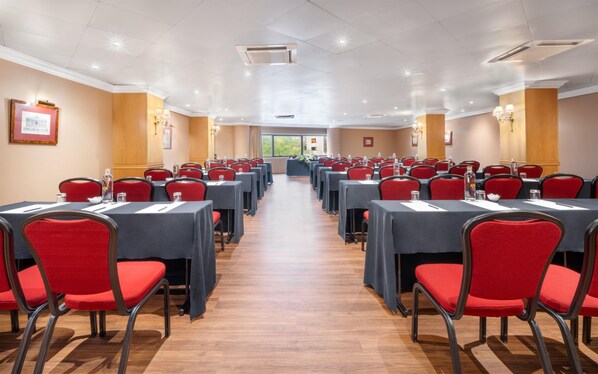 A conference room with rows of tables and red chairs, equipped with water bottles and nameplates.