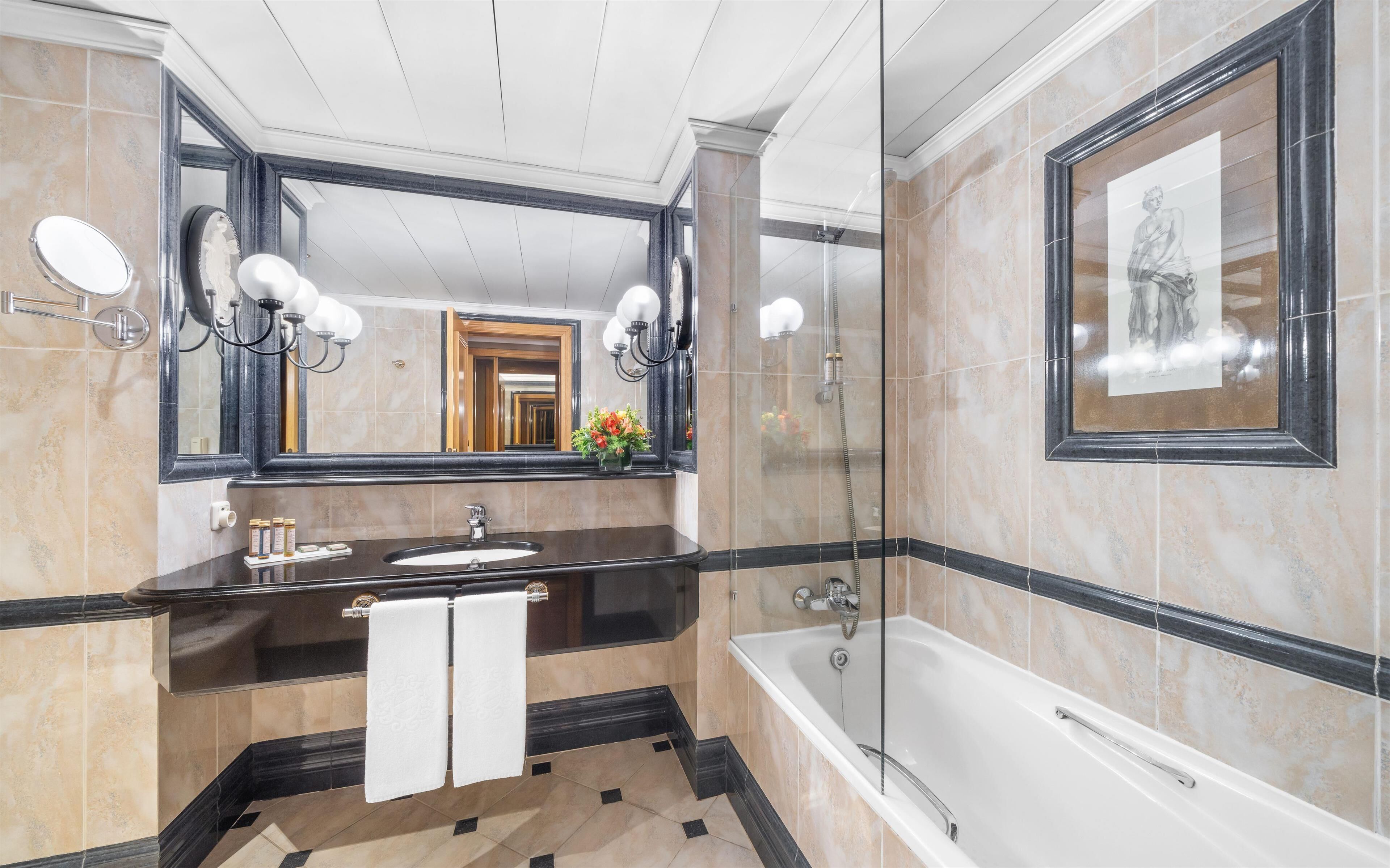 A luxurious bathroom with a large mirror, a bathtub, and a vanity with a sink.