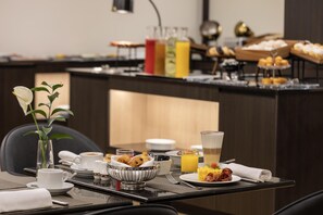 Un bufé de desayuno con diversas opciones de comida, una estación de café y una barra de zumos.