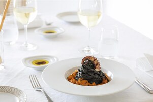 A white table with a plate of pasta, a fork, and wine glasses.