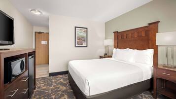 A hotel room with a large bed, a television, a desk with a lamp, and a picture on the wall.