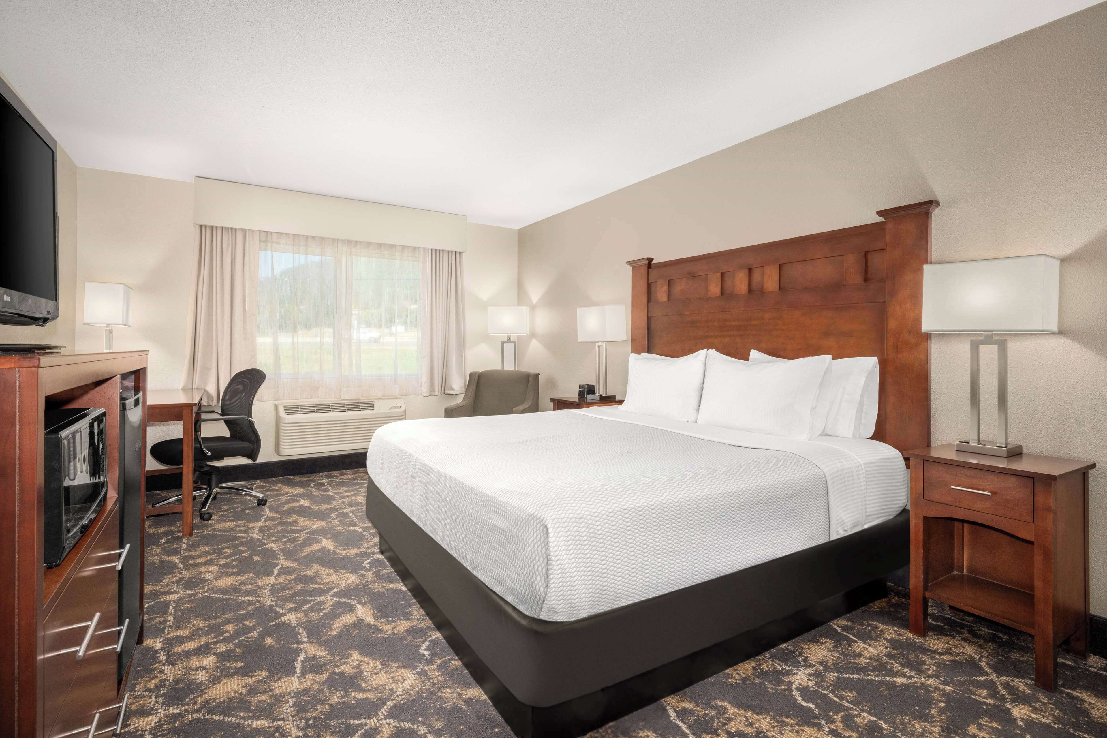 A hotel room with a large bed, a desk with a TV, a chair, and a lamp.