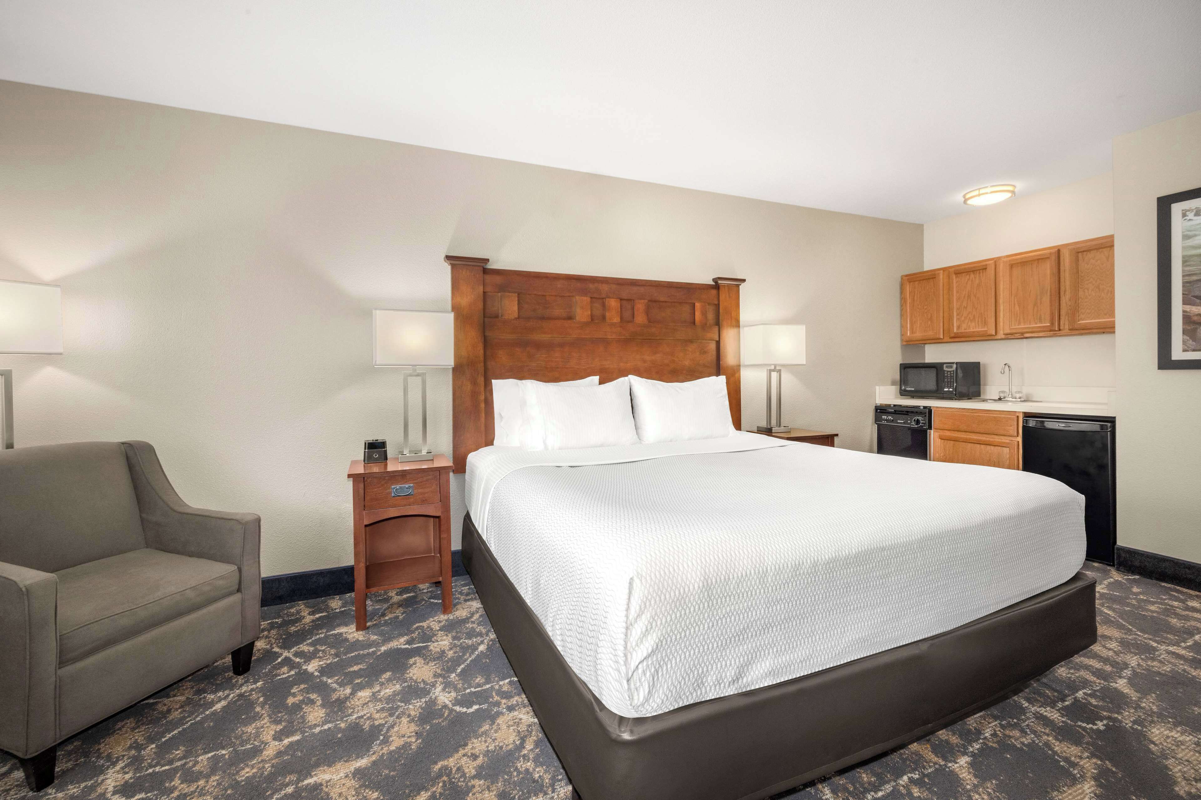 A hotel room with a large bed, a sofa, a nightstand, a lamp, a microwave, and a small kitchen area.