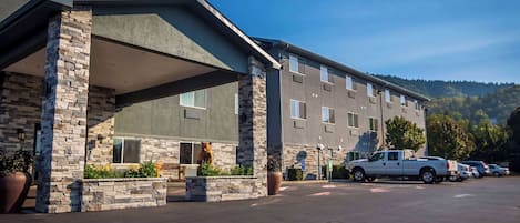 A hotel with a stone facade, a covered entrance, and a parking lot with a white pickup truck.