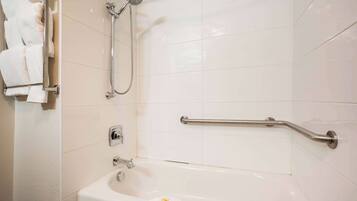 A bathroom with a bathtub, a shower, and a handrail.