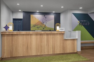 Una recepción de hotel con diseño moderno, que presenta una barra de madera, un cuadro abstracto grande y un letrero con el nombre del hotel y sus reconocimientos.
