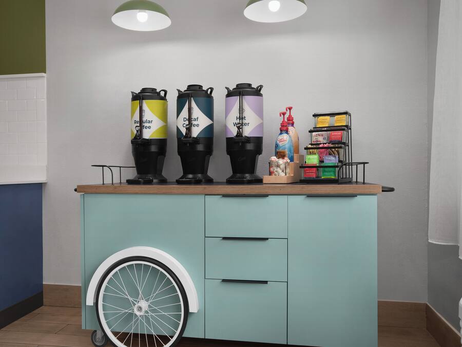 En köksbänk med fyra kaffebryggare, en dispenser för flytande tvål och en liten hylla med diverse föremål.