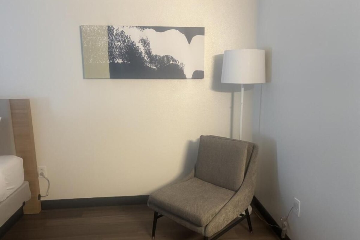 Een kamer met een bed, een stoel, een lamp en een kunstwerk aan de muur.