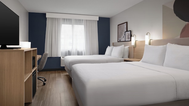 Een hotelkamer met twee bedden, een bureau, een stoel, een televisie en een raam met gordijnen.