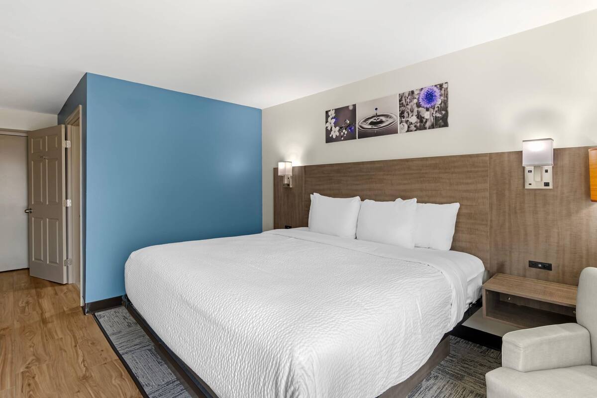 A hotel room with a large bed, a blue accent wall, a wooden headboard, and two wall-mounted light fixtures.