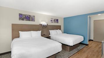 A hotel room with two beds, a nightstand, a wall-mounted lamp, and artwork on the wall.