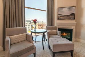 A hotel room with two armchairs, a small round table with a vase of flowers, a fireplace, and a city view through large windows. - The Magnolia Hotel and Spa (Victoria)