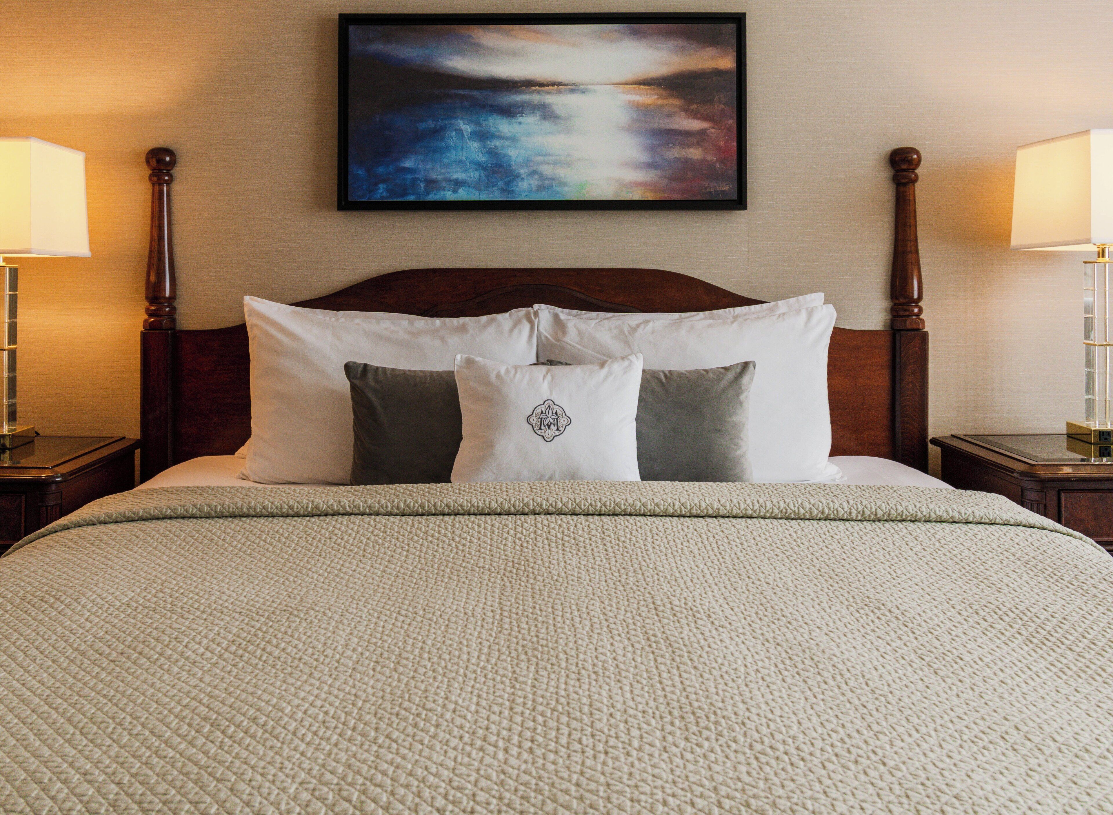 A neatly made bed with a quilted cover, a wooden headboard, and two bedside lamps.