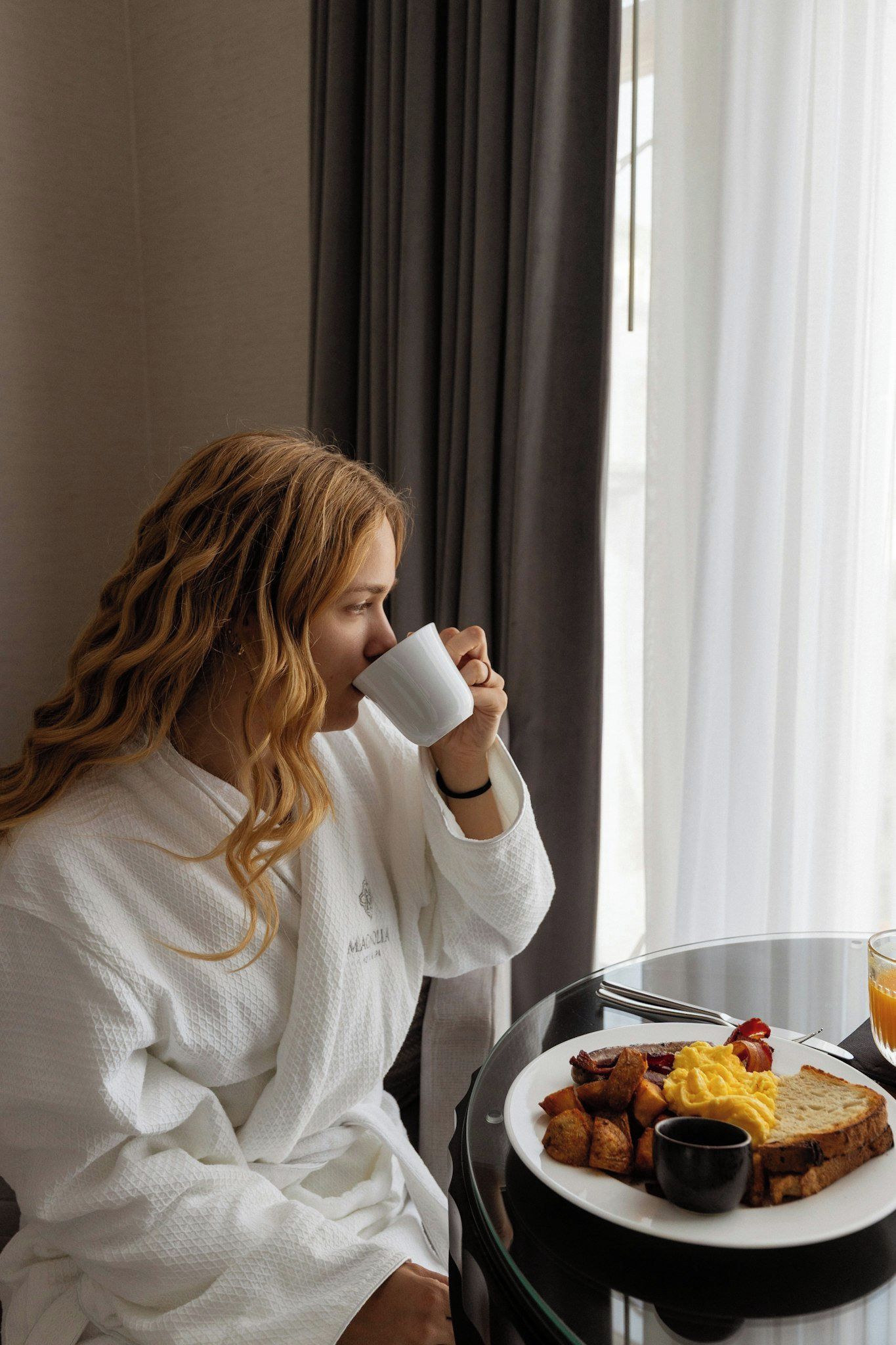 A person seated at a table with a breakfast plate containing toast, eggs, bacon, and potatoes.