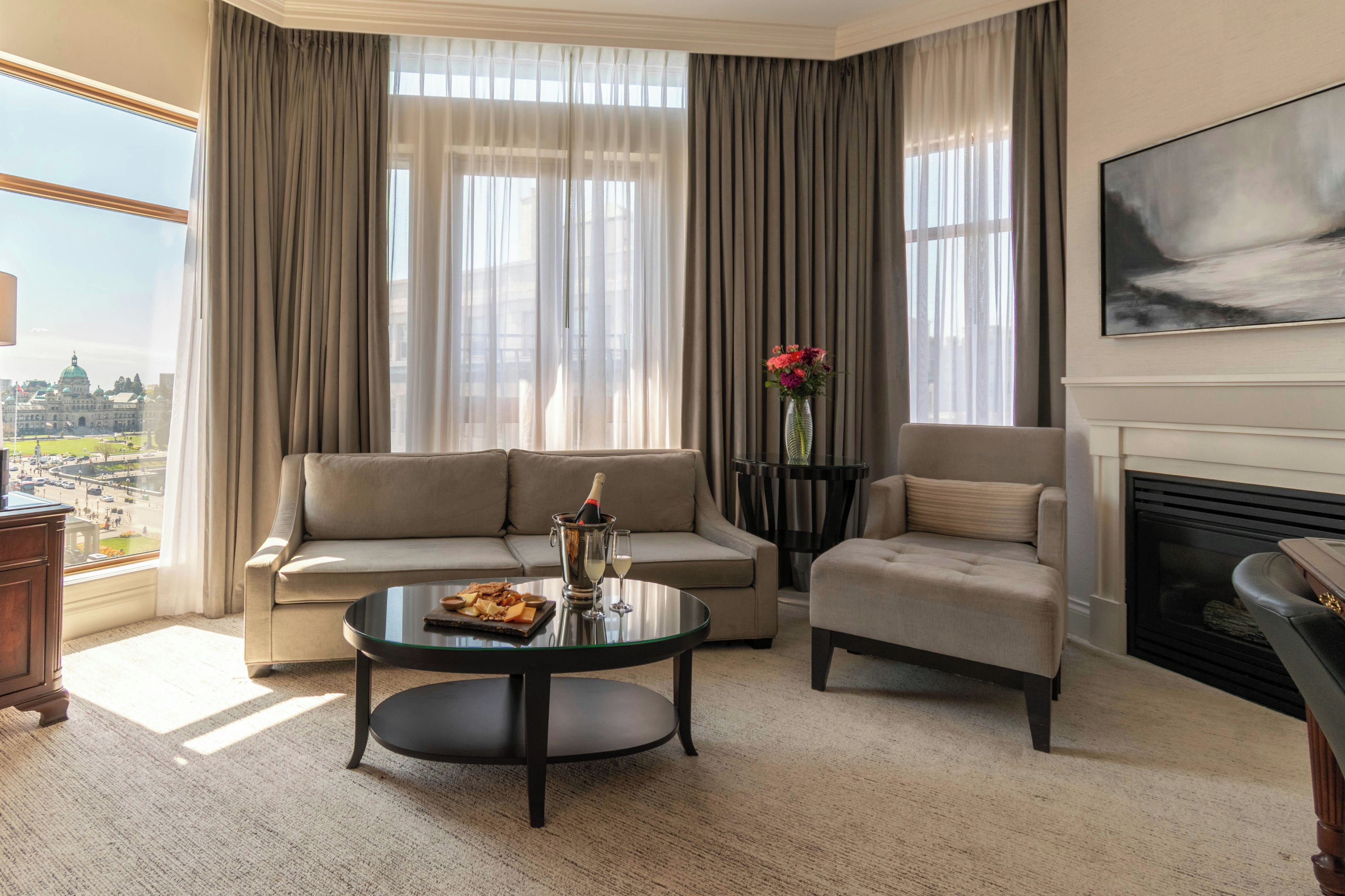 Un salon comprenant un canapé, un fauteuil et une table basse, une cheminée et une grande fenêtre avec des rideaux.