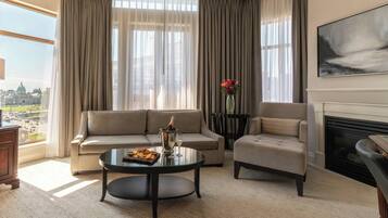 Un salon comprenant un canapé, un fauteuil et une table basse, une cheminée et une grande fenêtre avec des rideaux.