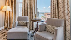 A hotel room with two armchairs, a lamp, a table with a bottle, and a view of the cityscape.