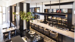 A modern bar area with a long counter, bar stools, and a variety of bottles.