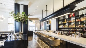 A modern bar area with a long counter, bar stools, and a variety of liquor bottles.