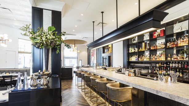 Un espace bar moderne, doté d’un long comptoir, de tabourets et d’une variété de bouteilles d’alcool.