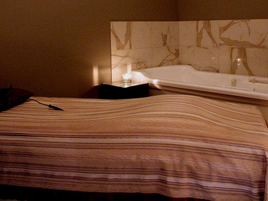 A hotel room with a bed, a bedside table, a lamp, and a bathtub.