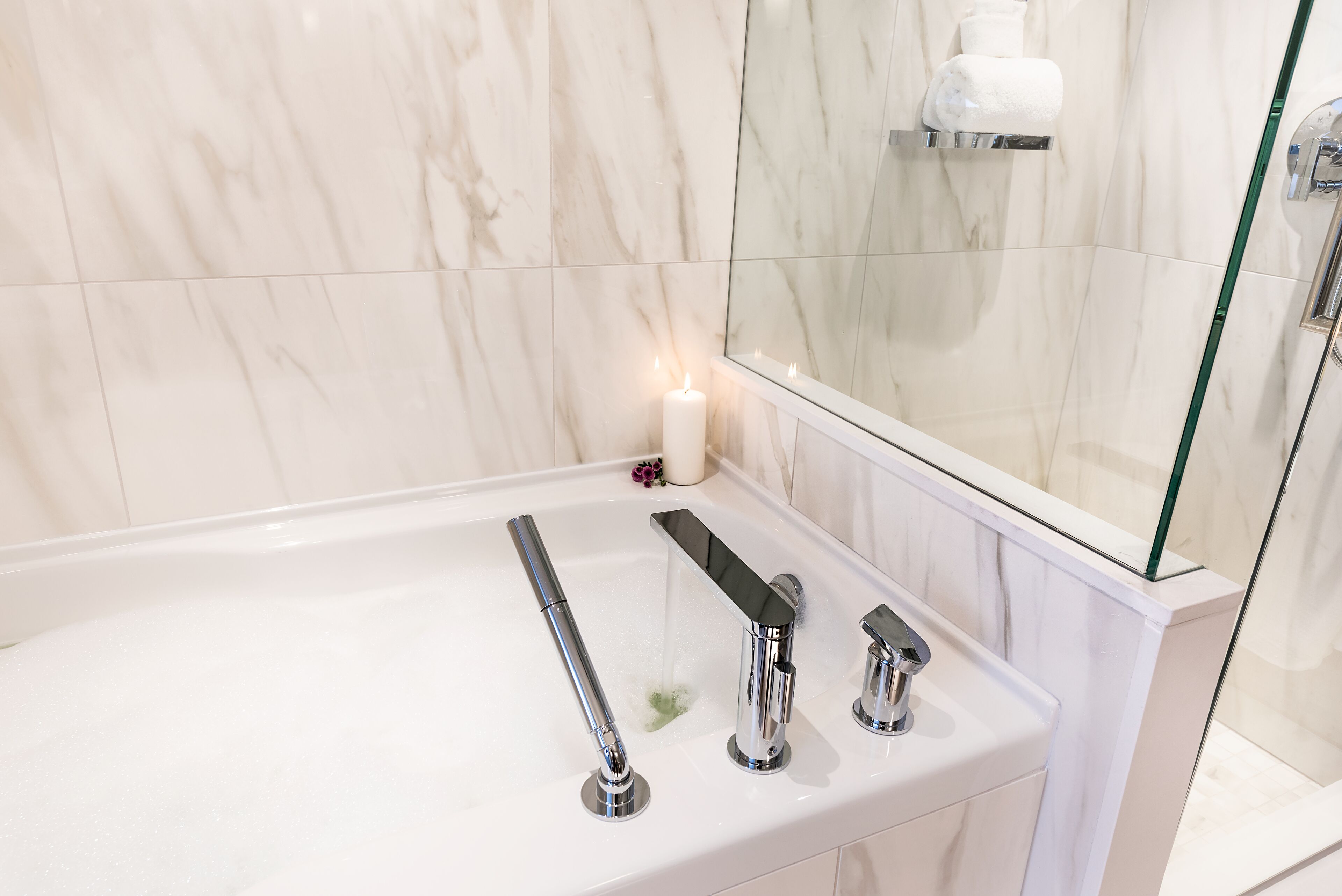 A modern bathroom with a white marble sink, three faucets, and a glass shower enclosure.