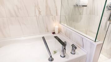 A modern bathroom with a white marble sink, three faucets, and a glass shower enclosure.