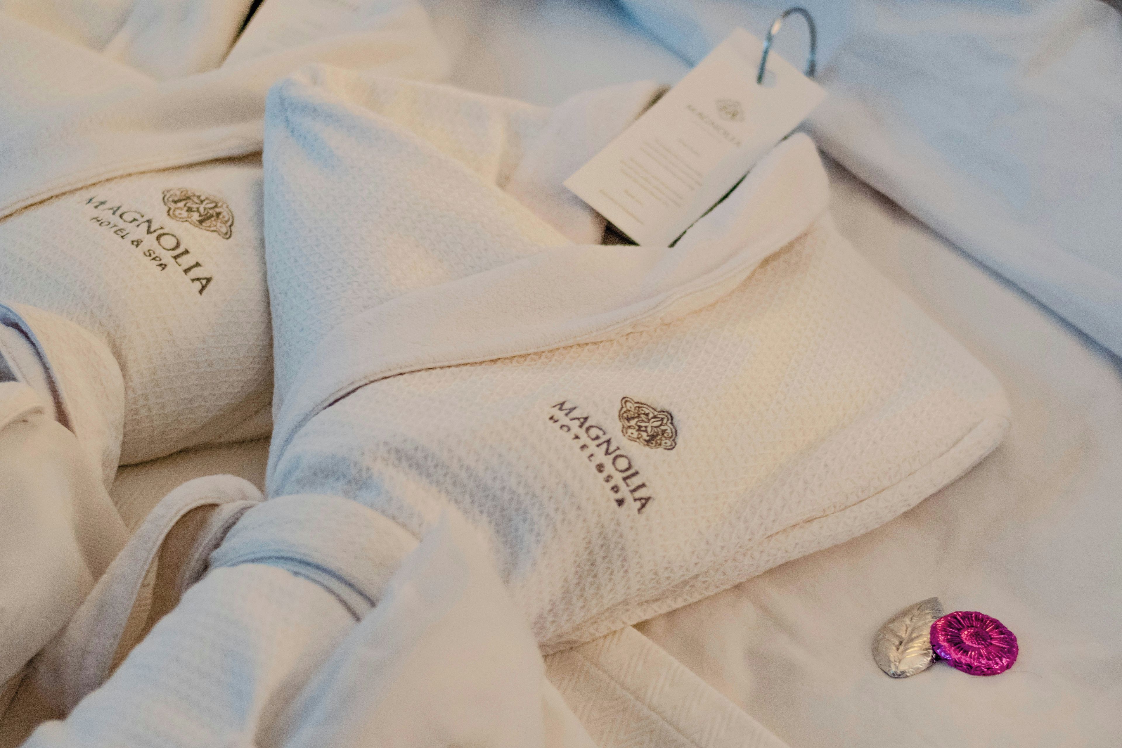 Un ensemble de serviettes blanches ornées du logo « Magnolia Hotel & Spa », ainsi qu’une étiquette et un petit objet décoratif rose.