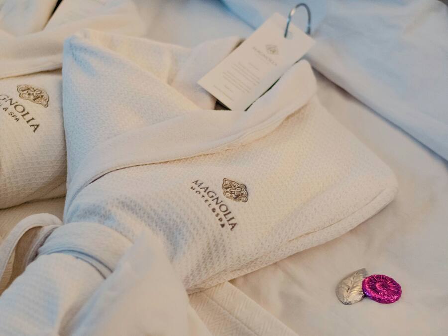 Un ensemble de serviettes blanches ornées du logo « Magnolia Hotel & Spa », ainsi qu’une étiquette et un petit objet décoratif rose.