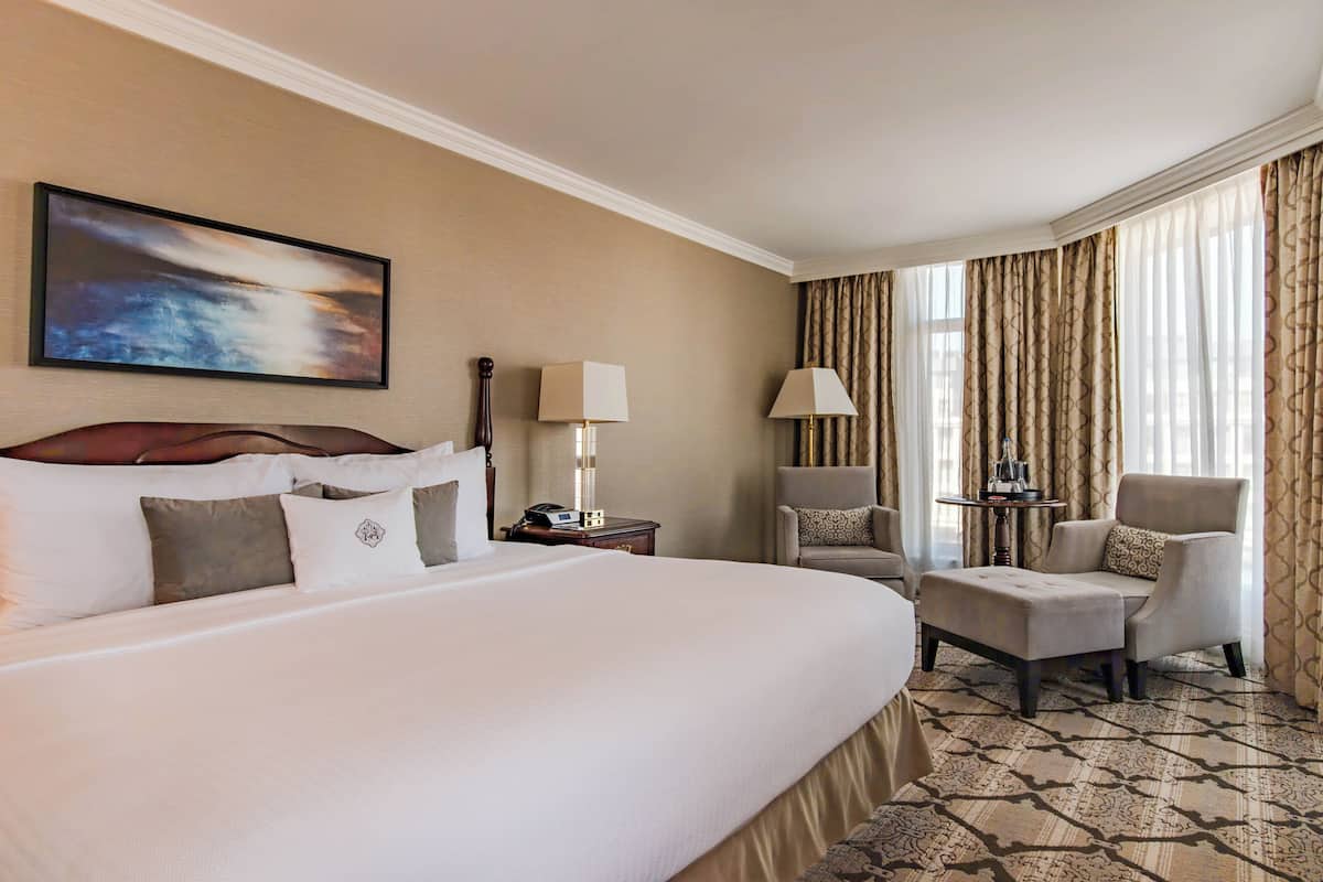 Habitación de hotel con una cama grande, dos sillones, una mesita y un cuadro en la pared.