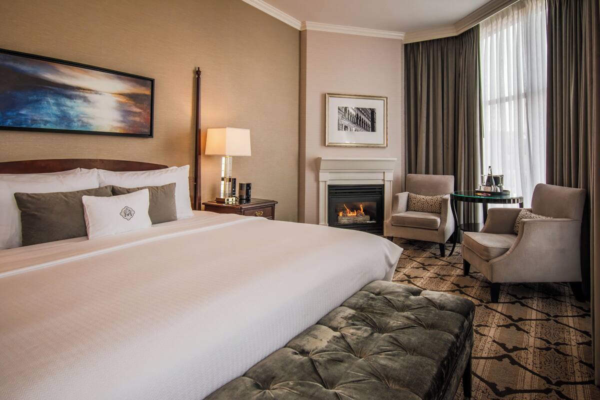 Habitación de hotel con una cama grande, chimenea, zona de estar con sillones y un cuadro en la pared.