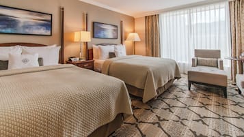 A hotel room with two beds, a chair, a desk, and a large window with curtains.